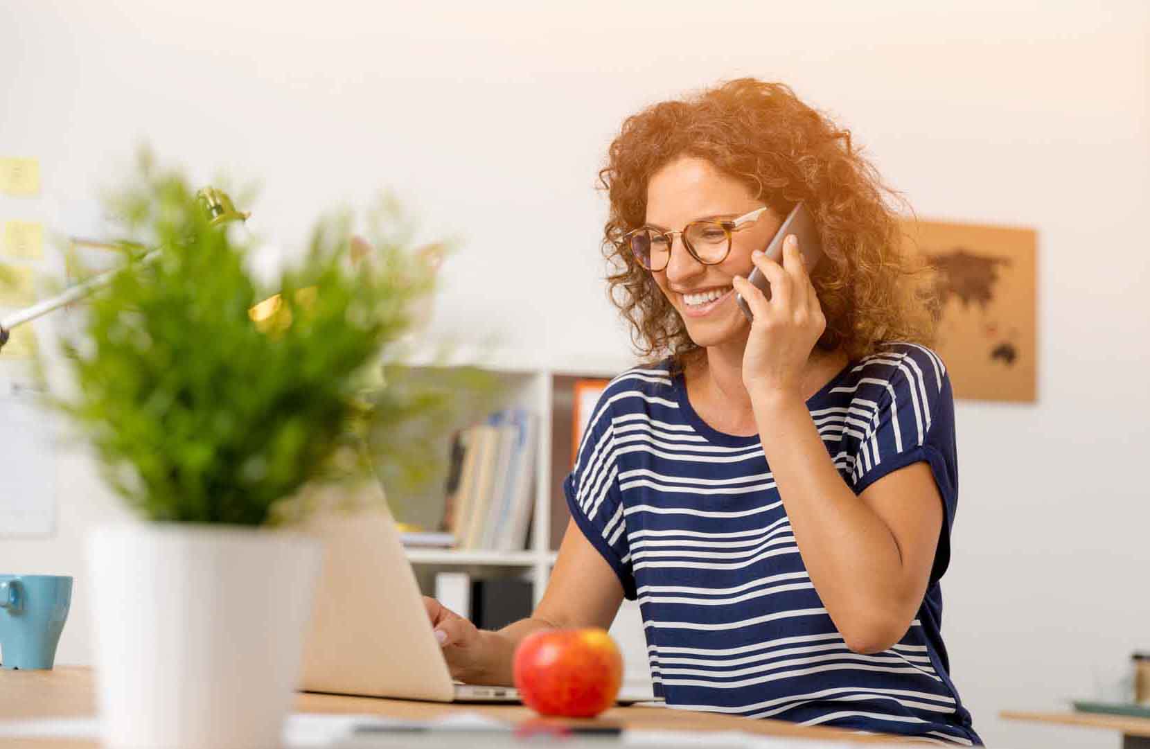 Femme souriante au téléphone devant son ordinateur